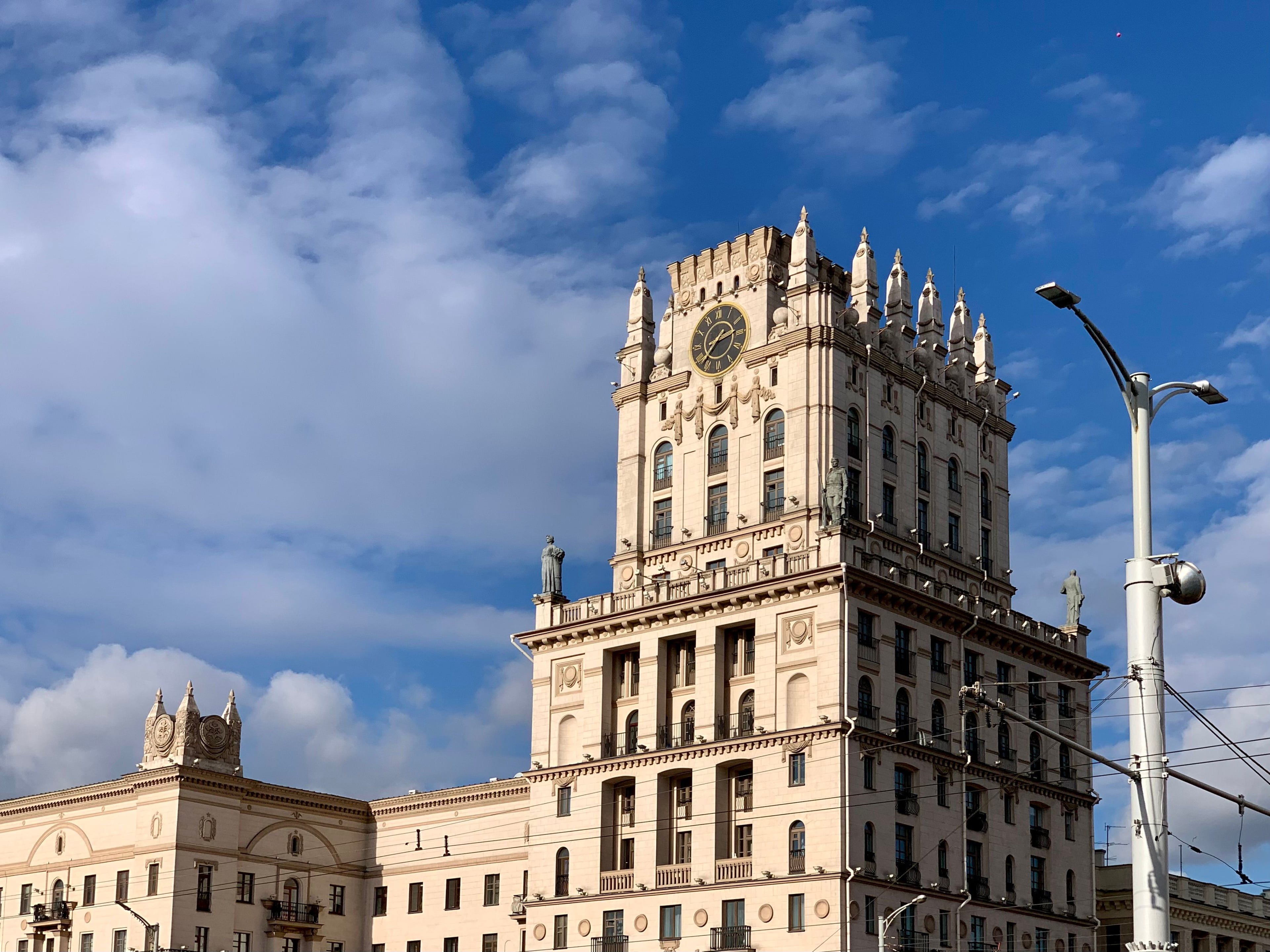 Башня с часами и скульптурами на Привокзальной площади в Минске на фоне синего неба с облаками